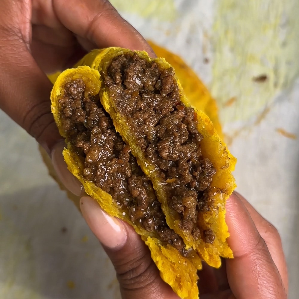 Close-up of a hot Jamaican beef patty with flaky pastry and steam rising from the filling