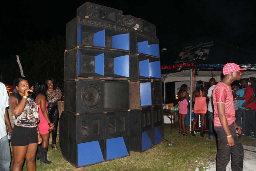 A tall blue-and-black speaker stack surrounded by people at an outdoor night event.
