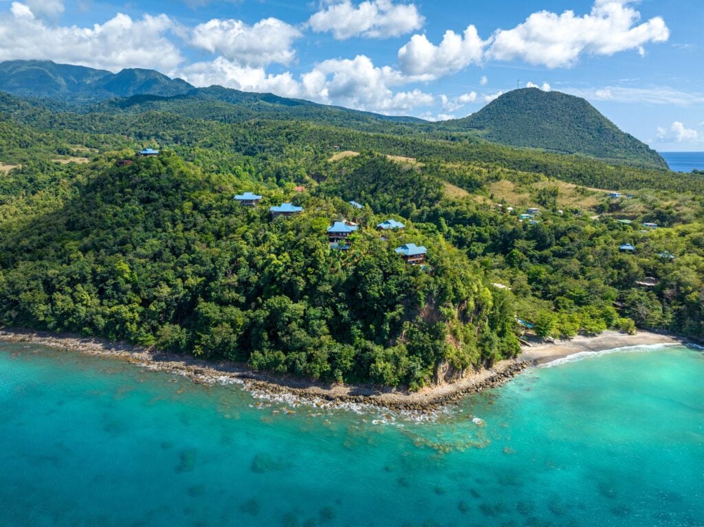 Aerial view of forested coastal hills, scattered villas and turquoise sea at Secret Bay in Dominica.