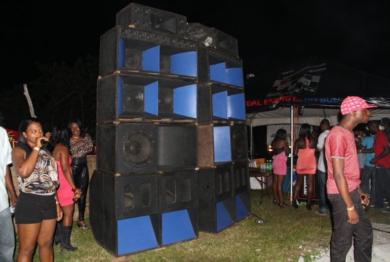 A tall blue-and-black speaker stack surrounded by people at an outdoor night event.