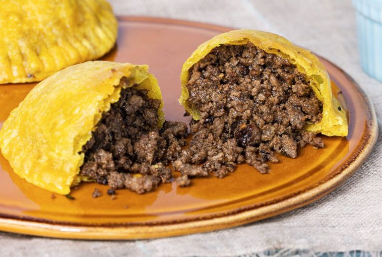 Close-up of a hot Jamaican beef patty with flaky pastry and steam rising from the filling