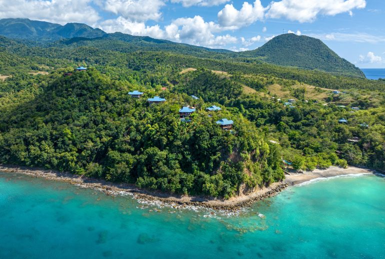 Aerial view of forested coastal hills, scattered villas and turquoise sea at Secret Bay in Dominica.